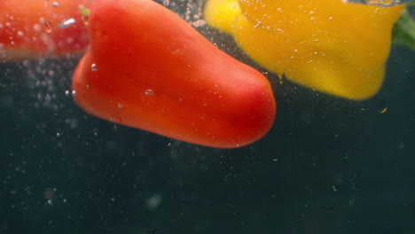 Close-up-several-cut-slices-of-fresh-green-and-yellow-red-bell-pepper-thrown-and-floating-in-clear-transparent-water-low-angle-side-view-slow-motion
